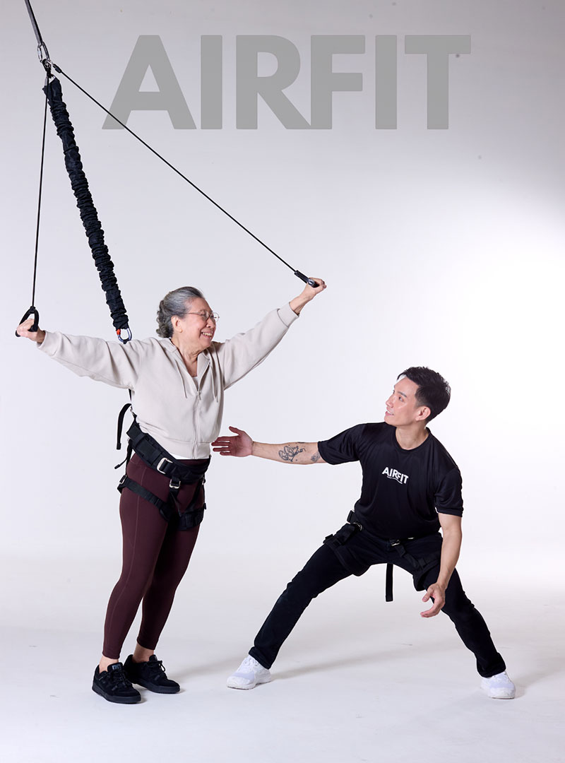 Senior woman performing bungee fitness exercise with professional trainer using suspension resistance system